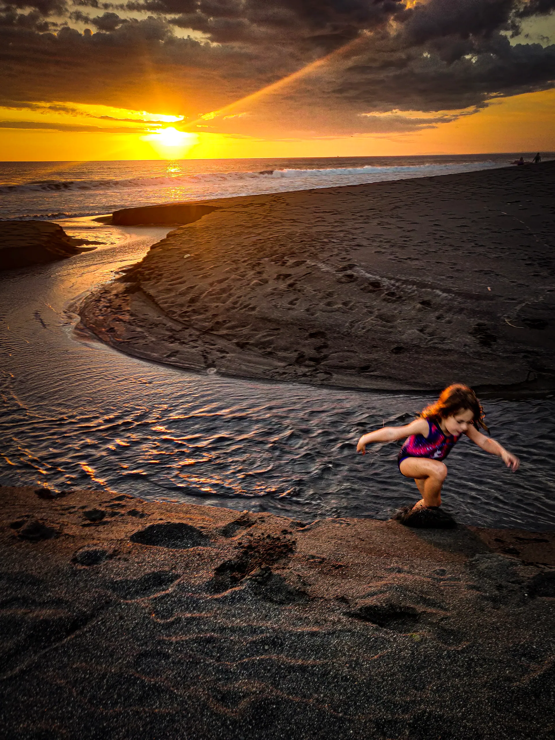 Child playing at sunset on Playa Hermosa with a stream meeting the Pacific