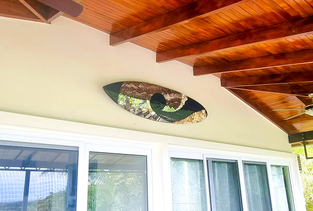 Surfboard mosaic art piece mounted on the deck wall under exposed wood beams